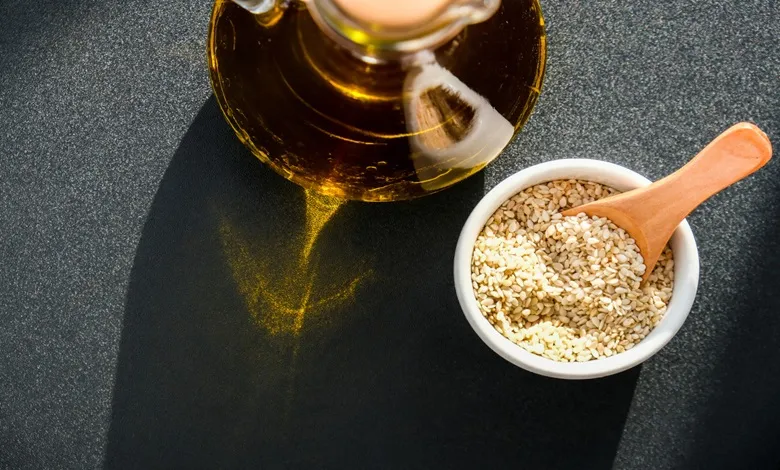 عکس از یک کاسه کنجد که درون آن قاشق است و یک شیشه روغن کنجد