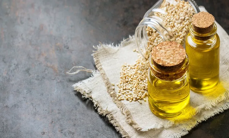 عکس از دو شیشه با درب بسته روغن کنجد و کمی کنجد در یک شیشه بر روی پارچه